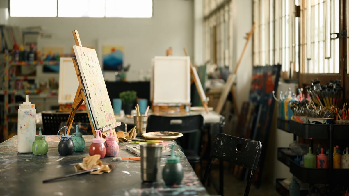 Sunlit art studio with easels, paint-splattered tables and pigment bottles