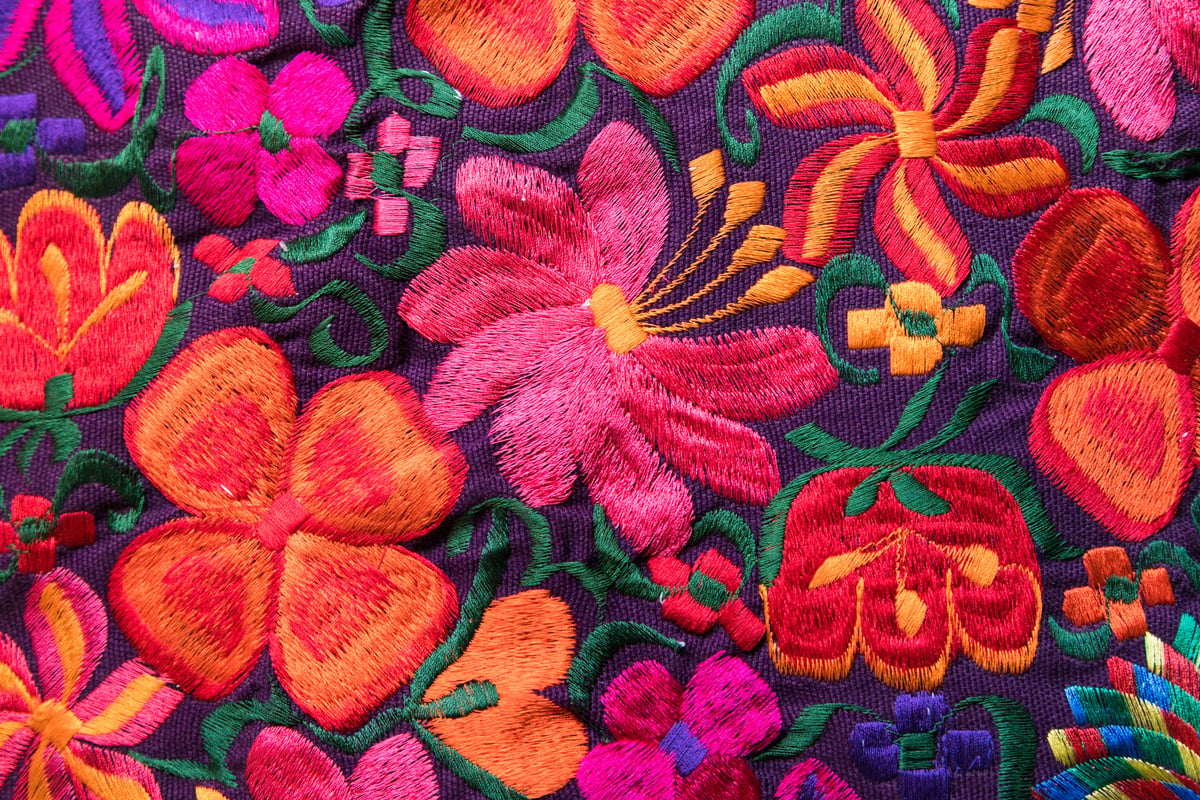 Close-up texture of colourful handmade floral embroidery on dark fabric