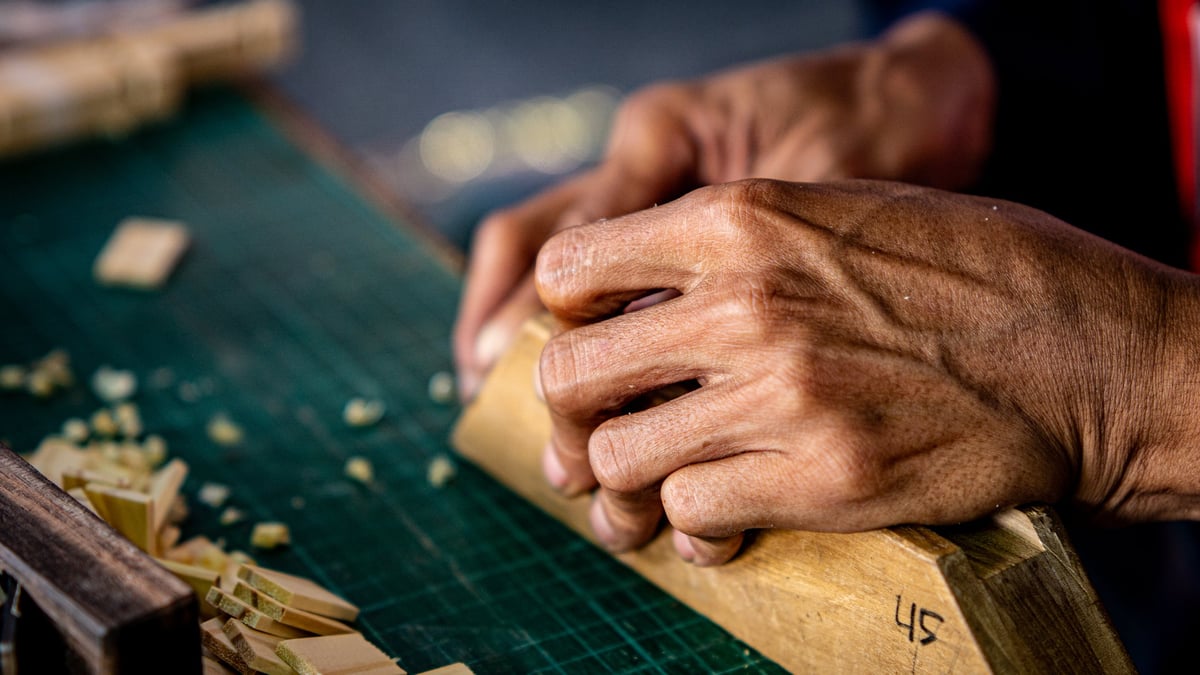 Close-up of a craftsperson's hands shaping a piece of wood at the workbench