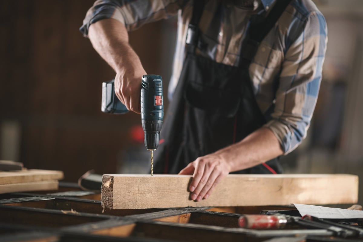 Carpenter at work in a wood workshop, drilling into a timber plank