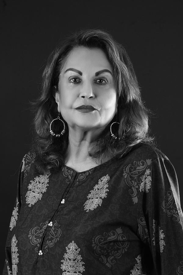 Black and white portrait of Nighat Bokhari with shoulder-length dark hair, wearing ornate patterned clothing and dangling hoop earrings against a dark background