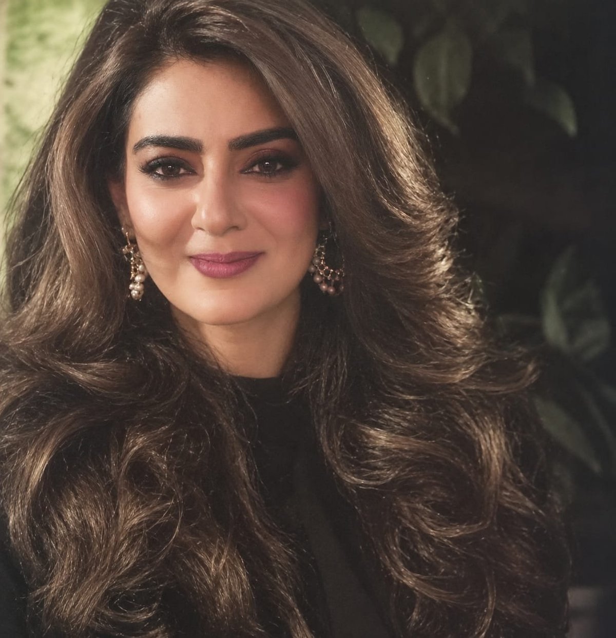 Nageen Rizvi — Heart of Chahek — portrait of a woman with long dark wavy hair, wearing pink lipstick and pearl drop earrings against a blurred background